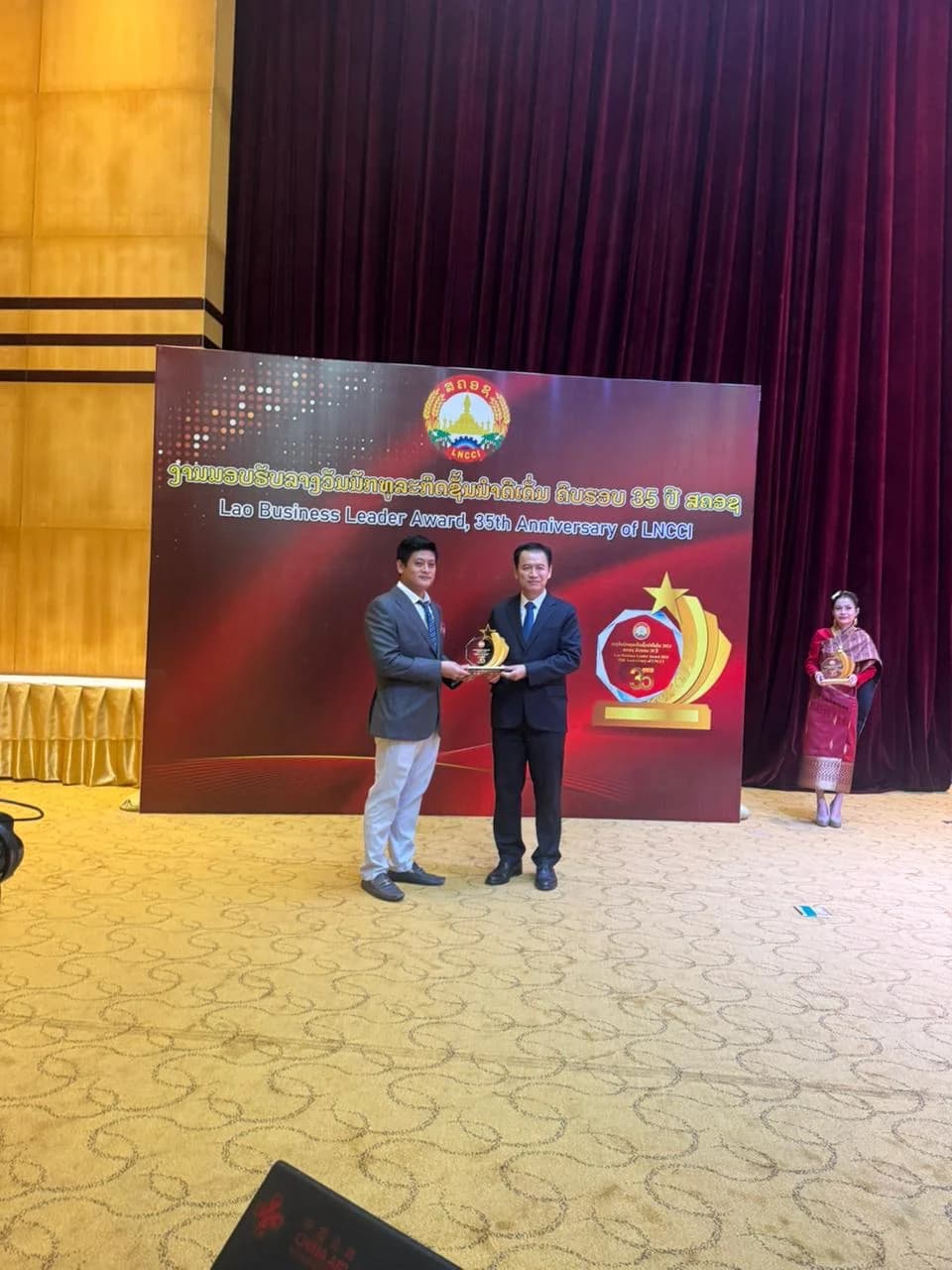 ທ່ານ ຄຳໝິງ ສີລາຊາ ຮອງປະທານ ບໍລິສັດ ກຸ່ມດວງຈະເລີນ ພັດທະນາກໍ່ສ້າງ ຈຳກັດຜູ້ດຽວ ຂຶ້ນຮັບລາງວັນ ນັກທຸລະກິດຊັ້ນນຳດີເດັ່ນ ຄົບຮອບ 35 ປີ ສຄອຊ 